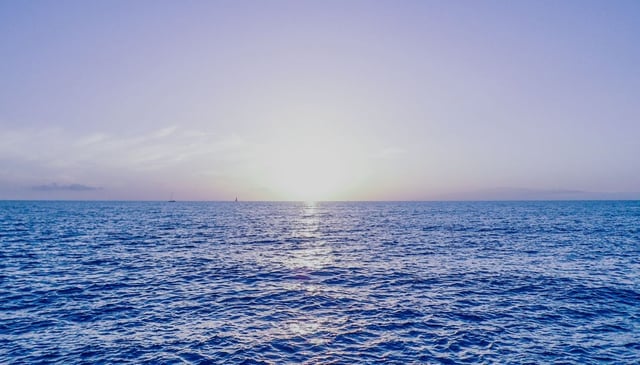 Low sun on the horizon, casting a bright reflection on the water's surface, and with gentle waves